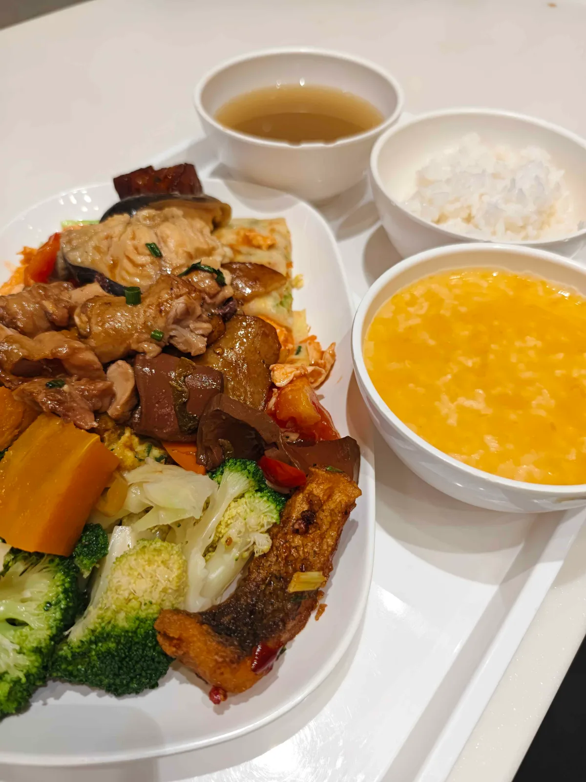 A canteen tray of rice, greens and braised dishes on a steel counter