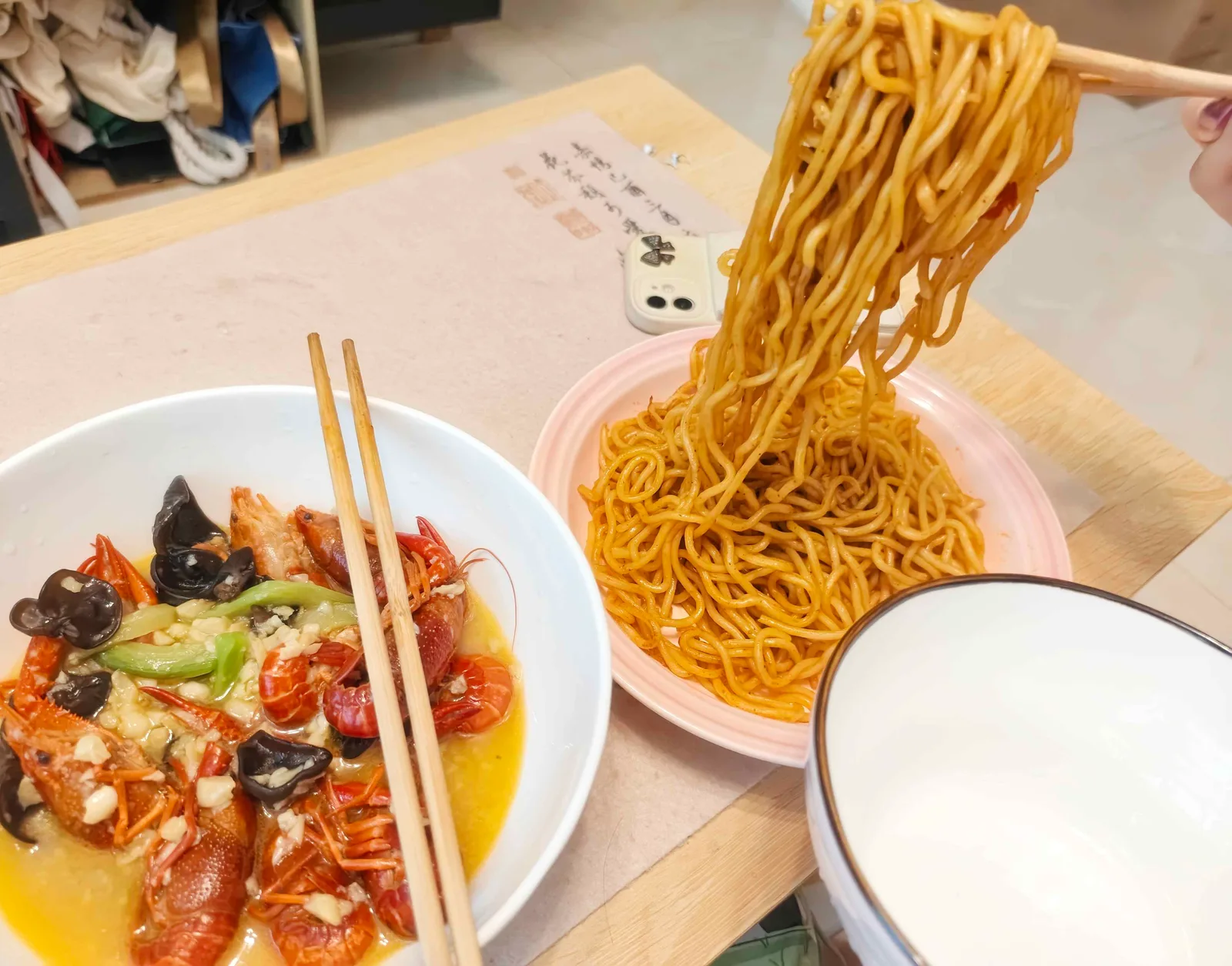 Chopsticks lifting noodles beside a bowl of garlic crayfish