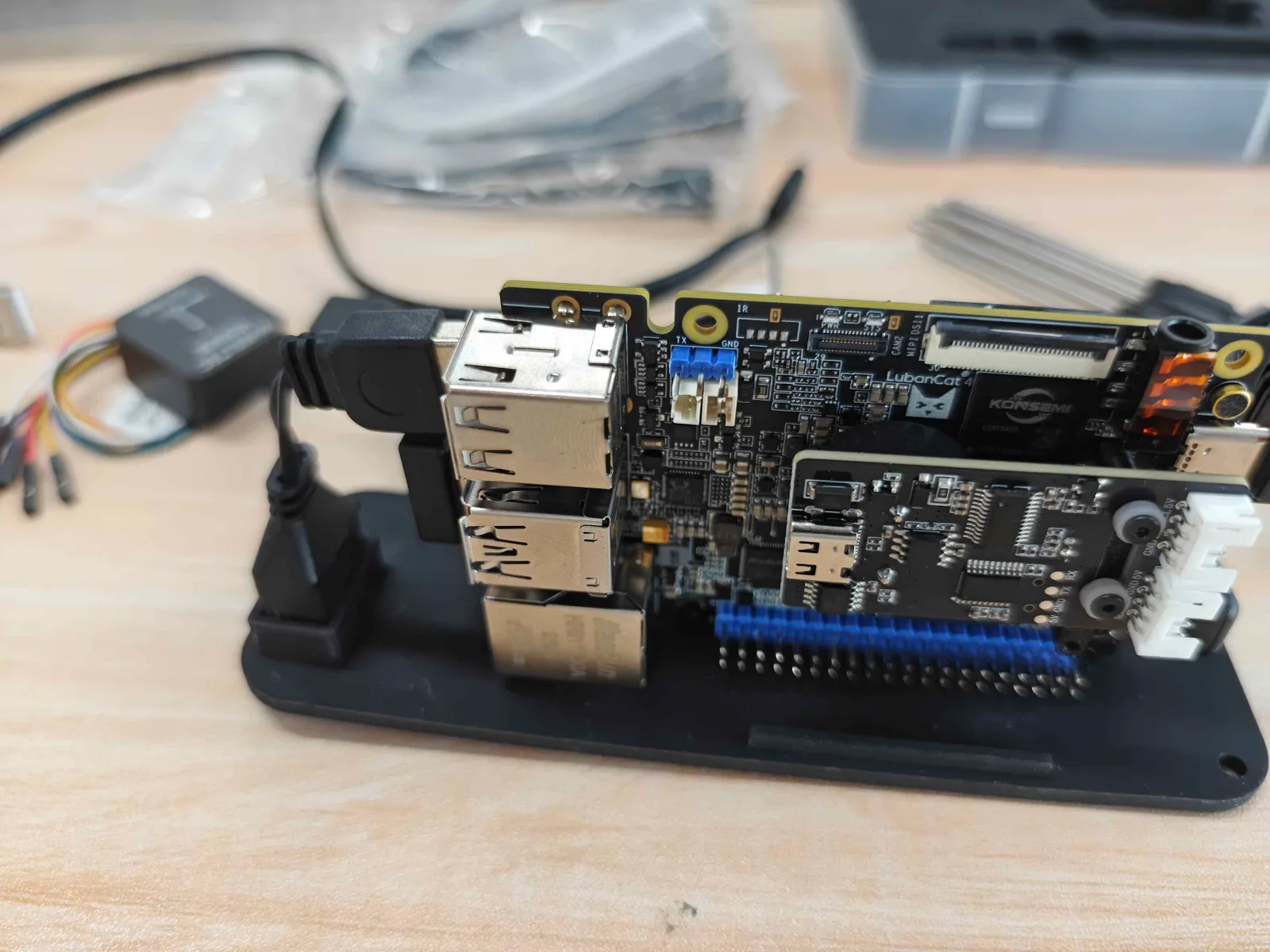 Two stacked single-board computers on a light wood desk, with USB ports, a pin header, jumper wires and a GPS module beside them.
