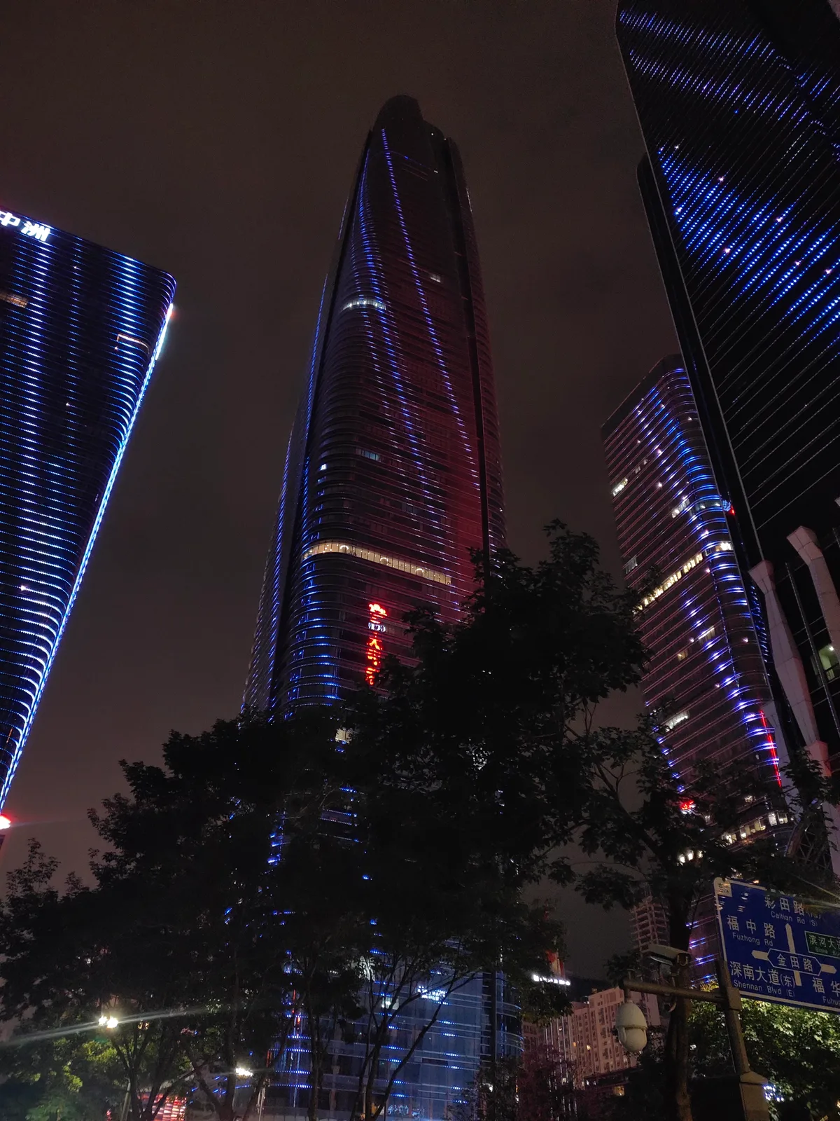 Shenzhen towers lit blue at night, seen from street level